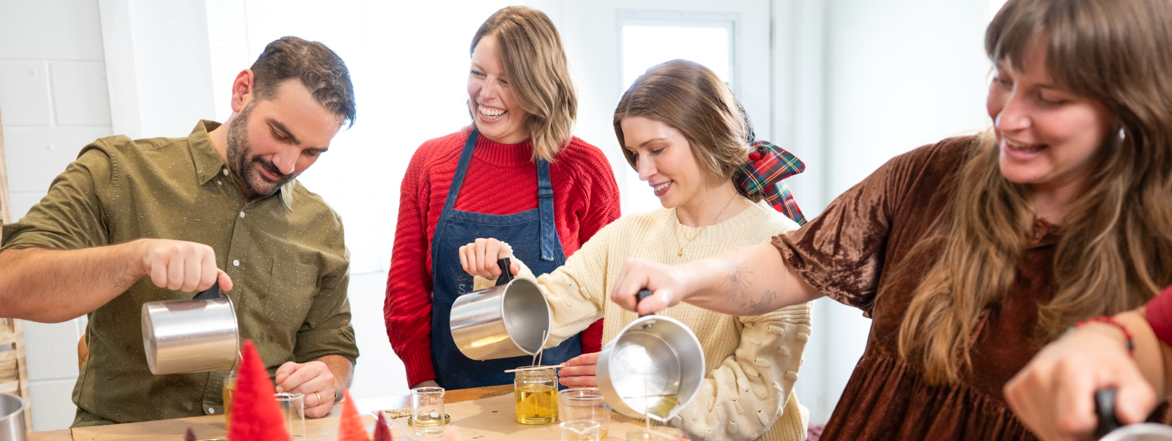 Group of people participating in a craft activity with red tree-shaped decorations on a table.